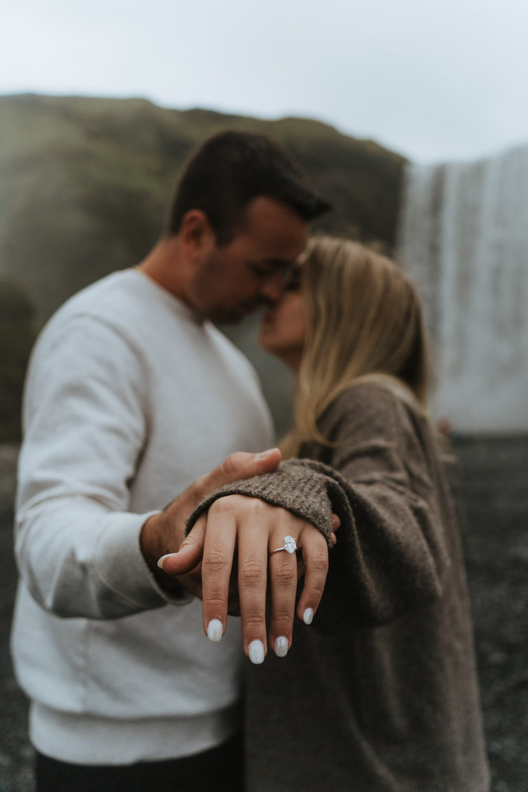 Girl showing ring to the camera while her fiancé is kissing her
