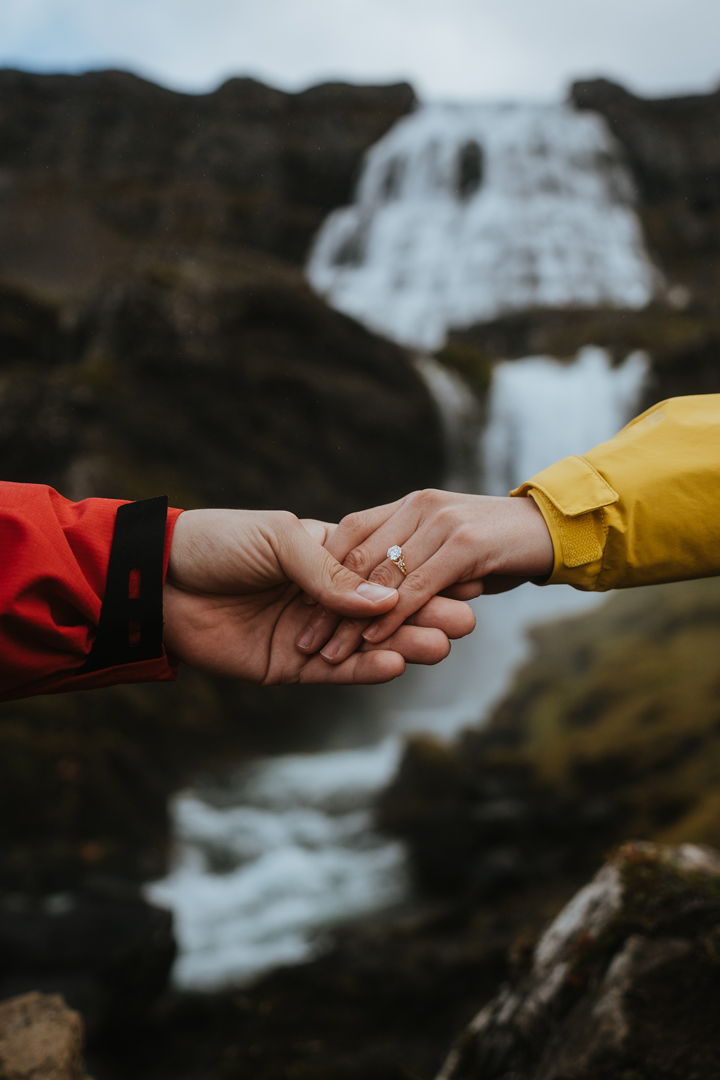 Couple showing their engagement ring with a Dynjandi waterfall background
